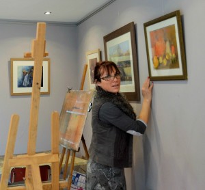 Léa dans son atelier. On réajuste les tableaux au murs 